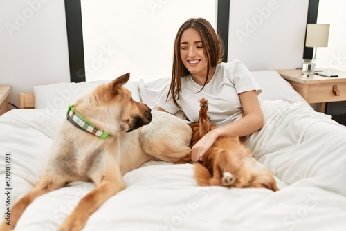 Photography Young hispanic woman playing with dogs lying on bed at bedroom