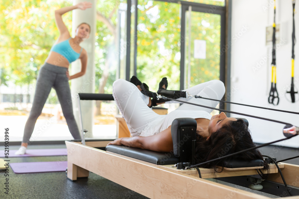 Hispanic woman pilates exercises on machines in a health club.