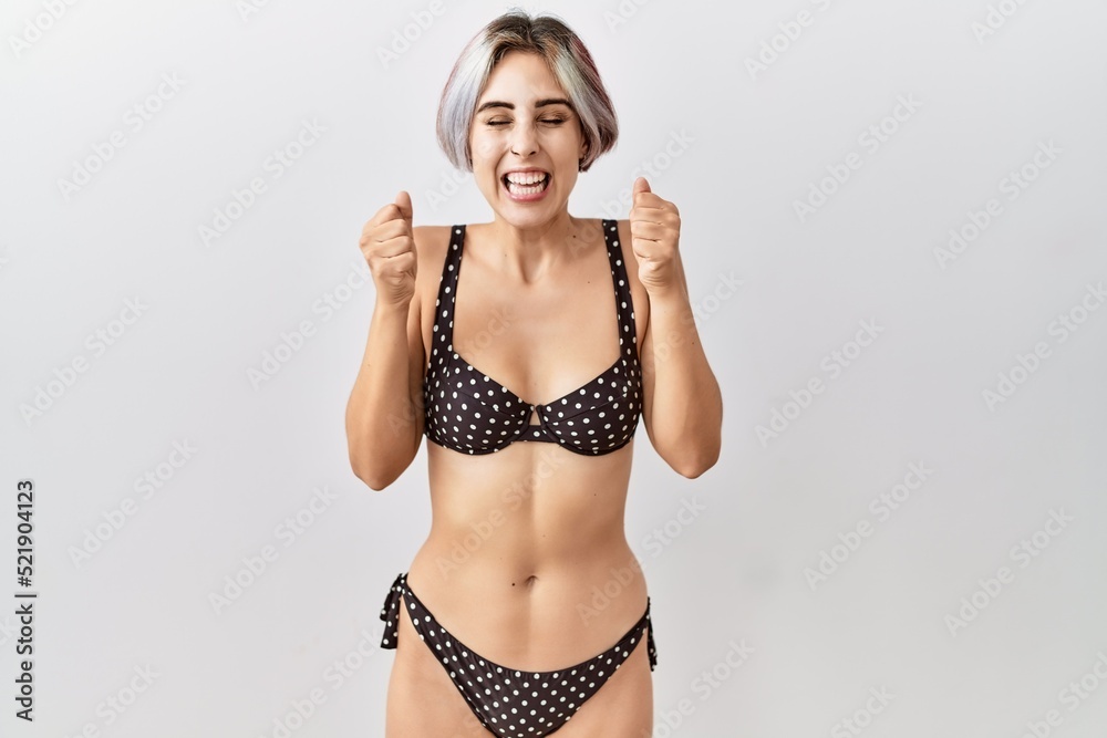 Naklejka premium Young beautiful woman wearing swimsuit over isolated background excited for success with arms raised and eyes closed celebrating victory smiling. winner concept.