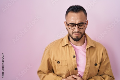 Young hispanic man standing over pink background with hand on stomach because nausea, painful disease feeling unwell. ache concept. © Krakenimages.com