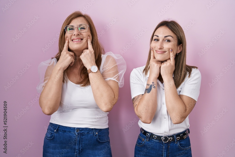 Hispanic mother and daughter wearing casual white t shirt over pink background smiling with open mouth, fingers pointing and forcing cheerful smile Hispanic mother and daughter wearing casual white t shirt over pink background smiling with open mouth, fingers pointing and forcing cheerful smile