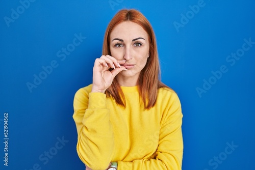 Young woman standing over blue background mouth and lips shut as zip with fingers. secret and silent, taboo talking