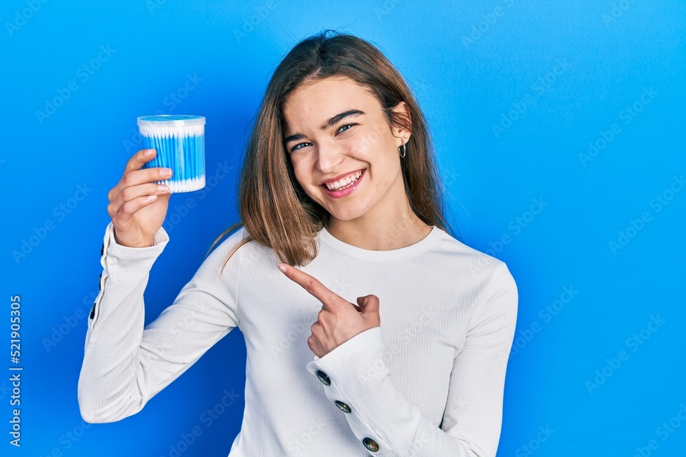 Young caucasian girl holding earwax cotton remover smiling happy pointing with hand and finger Young caucasian girl holding earwax cotton remover smiling happy pointing with hand and finger