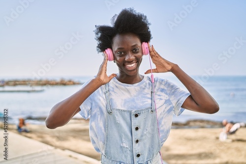 Young african woman listening to music using headphones by the sea
