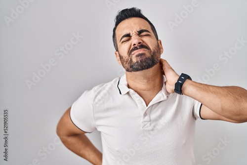 Young hispanic man with beard wearing casual clothes over white background suffering of neck ache injury, touching neck with hand, muscular pain