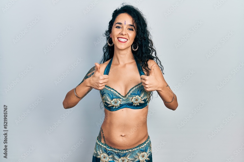 Fototapeta premium Young woman wearing bindi and traditional belly dance clothes success sign doing positive gesture with hand, thumbs up smiling and happy. cheerful expression and winner gesture.