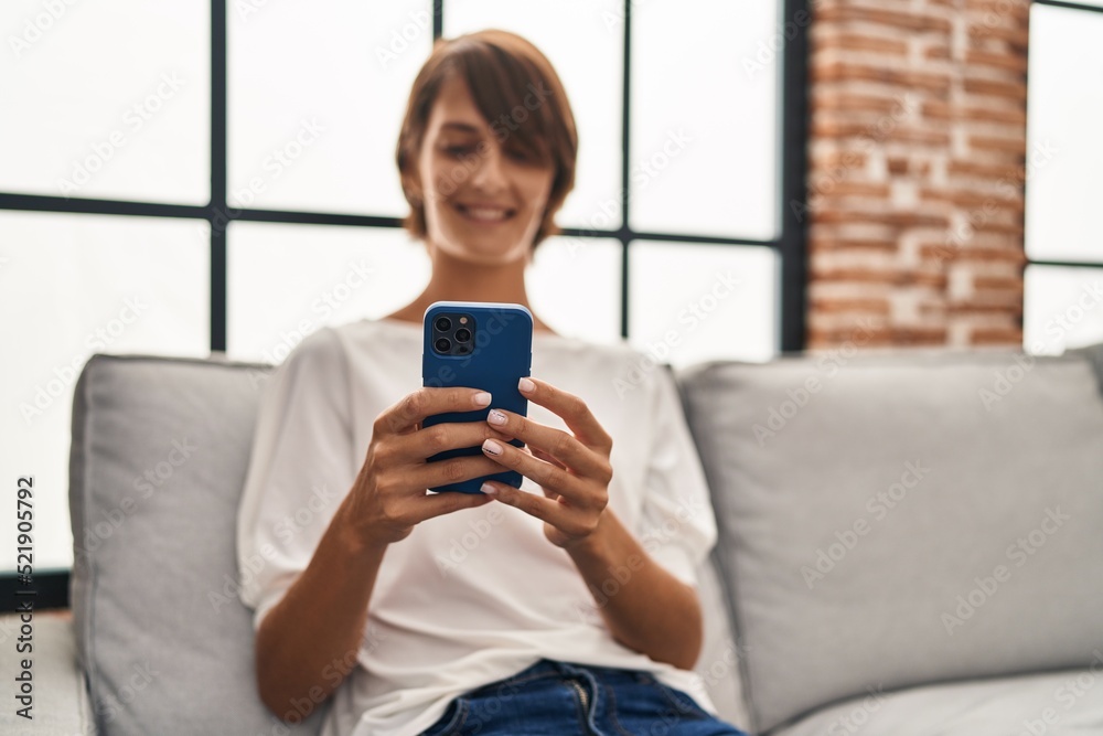 Young beautiful hispanic woman using smartphone sitting on sofa at home Young beautiful hispanic woman using smartphone sitting on sofa at home