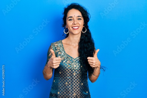 Young woman wearing bindi and traditional kurta dress success sign doing positive gesture with hand, thumbs up smiling and happy. cheerful expression and winner gesture.