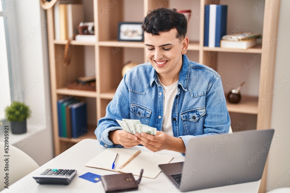 Fototapeta premium Young non binary man sitting on table counting dollars at home