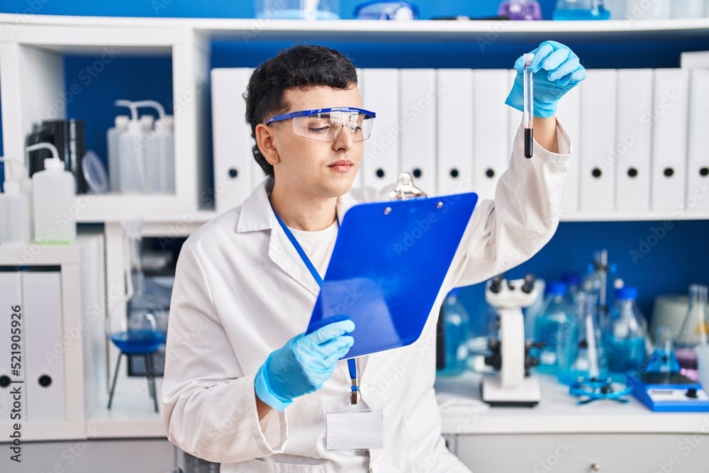 Fototapeta premium Young non binary man scientist reading report holding blood test tube at laboratory