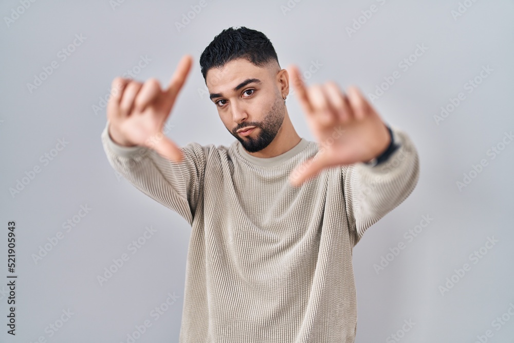 Fototapeta premium Young handsome man standing over isolated background doing frame using hands palms and fingers, camera perspective