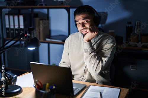 Young handsome man working using computer laptop at night looking stressed and nervous with hands on mouth biting nails. anxiety problem.