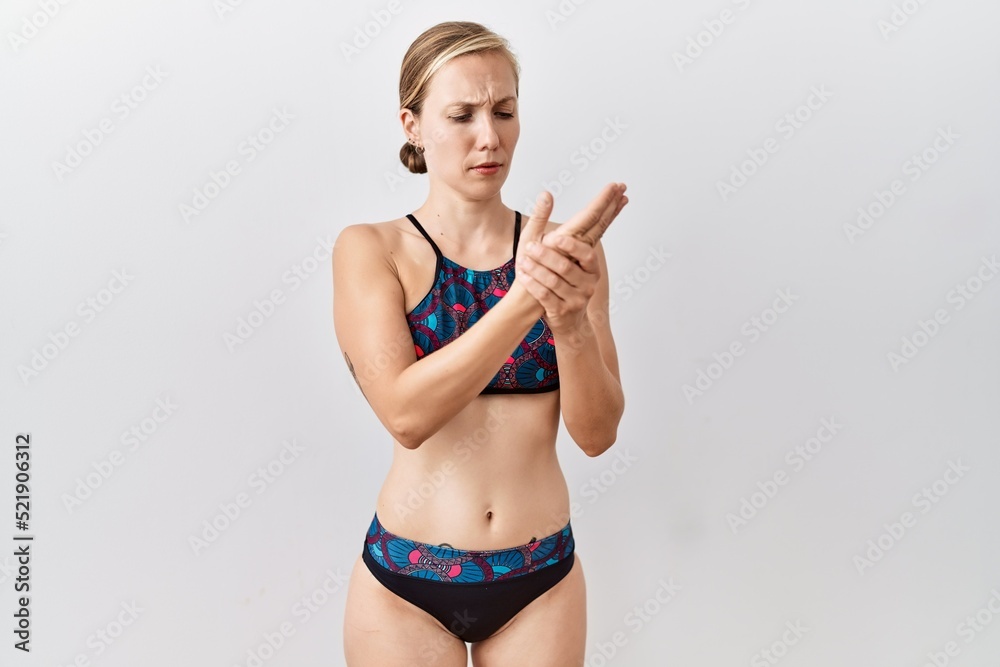 Young blonde woman wearing sporty bikini over isolated background suffering pain on hands and fingers, arthritis inflammation Young blonde woman wearing sporty bikini over isolated background suffering pain on hands and fingers, arthritis inflammation