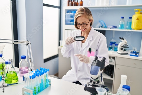 Young blonde woman scientist looking sample using loupe at laboratory
