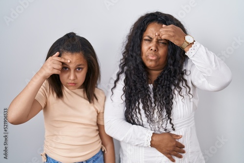 Mother and young daughter standing over white background pointing unhappy to pimple on forehead, ugly infection of blackhead. acne and skin problem photo