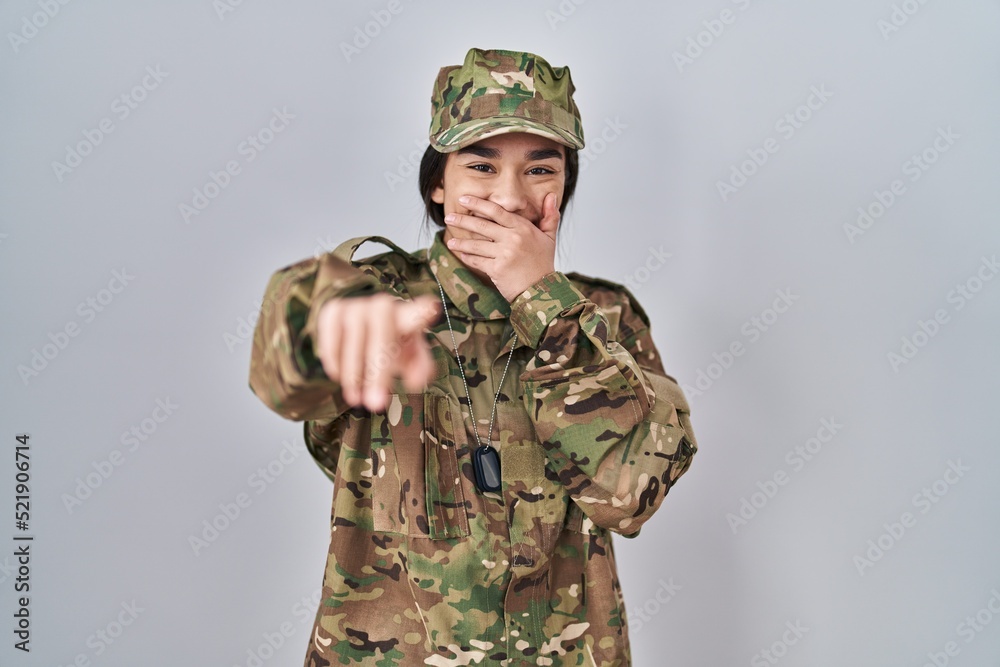 Young south asian woman wearing camouflage army uniform laughing at you, pointing finger to the camera with hand over mouth, shame expression Young south asian woman wearing camouflage army uniform laughing at you, pointing finger to the camera with hand over mouth, shame expression
