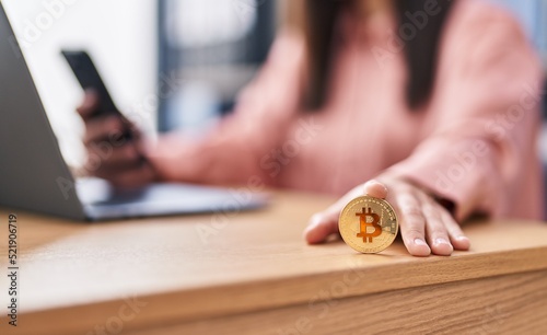 Young hispanic woman business worker using smartphone holding bitcoin at office