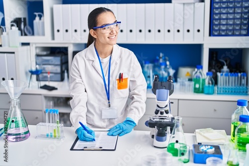 Young hispanic woman scientist writing on document working at laboratory