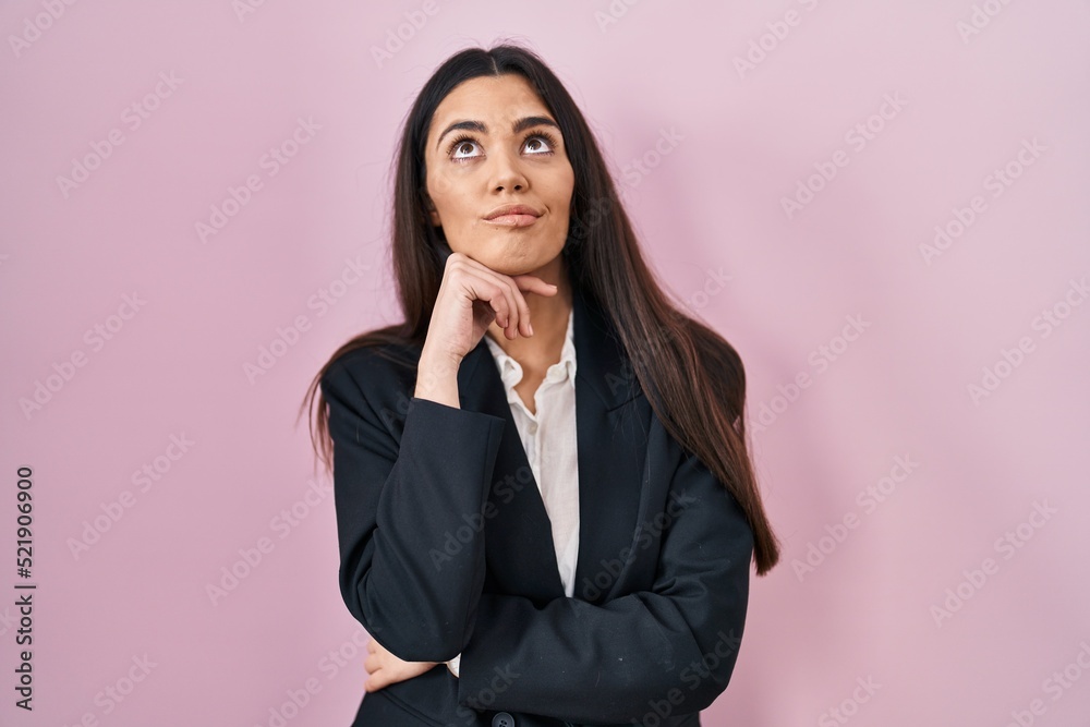 Young brunette woman wearing business style over pink background with hand on chin thinking about question, pensive expression. smiling with thoughtful face. doubt concept. Young brunette woman wearing business style over pink background with hand on chin thinking about question, pensive expression. smiling with thoughtful face. doubt concept.