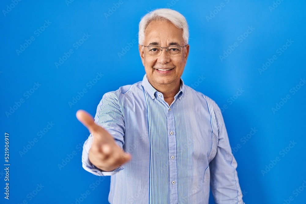 Hispanic senior man wearing glasses smiling cheerful offering palm hand giving assistance and acceptance. Hispanic senior man wearing glasses smiling cheerful offering palm hand giving assistance and acceptance.