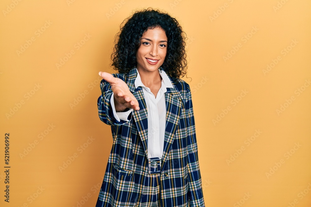 Young latin girl wearing business clothes smiling friendly offering handshake as greeting and welcoming. successful business. Young latin girl wearing business clothes smiling friendly offering handshake as greeting and welcoming. successful business.