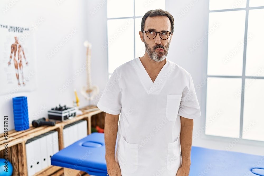 Middle age man with beard working at pain recovery clinic making fish face with lips, crazy and comical gesture. funny expression. Middle age man with beard working at pain recovery clinic making fish face with lips, crazy and comical gesture. funny expression.