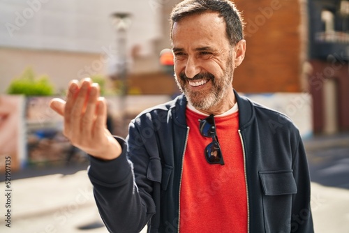 Middle age man smiling confident doing coming gesture with hand at street