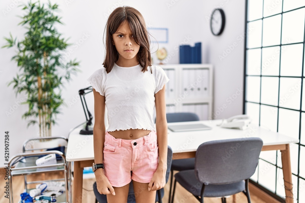 Young hispanic girl standing at pediatrician clinic skeptic and nervous, frowning upset because of problem. negative person. Young hispanic girl standing at pediatrician clinic skeptic and nervous, frowning upset because of problem. negative person.