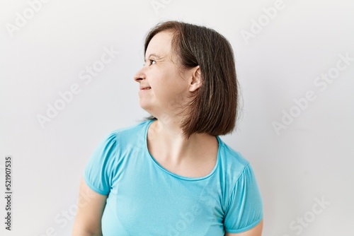 Young down syndrome woman standing over isolated background looking away to side with smile on face, natural expression. laughing confident.