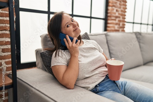 Down syndrome woman drinking coffee and talking on the smartphone at home