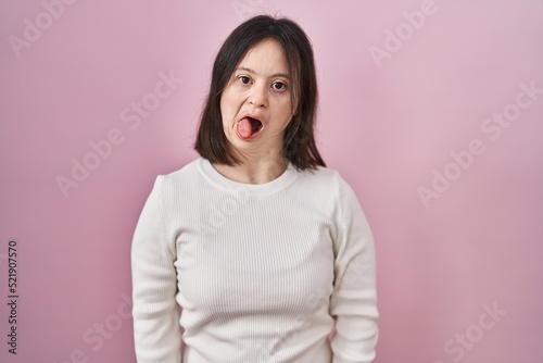 Woman with down syndrome standing over pink background sticking tongue out happy with funny expression. emotion concept. © Krakenimages.com