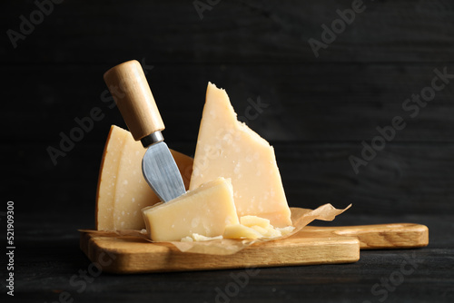 Pieces of Parmesan cheese and knife on black wooden table