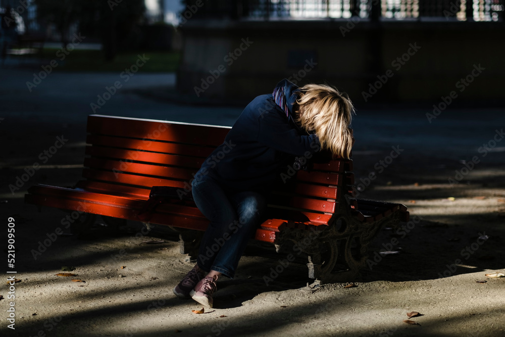 A woman is crying sitting on a bench in a summer park.