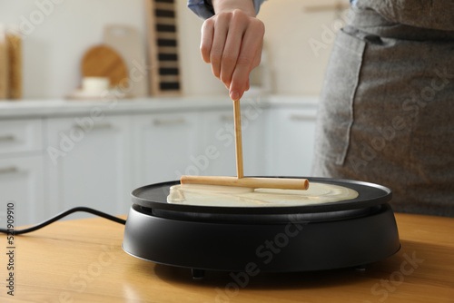 Woman cooking delicious crepe on electrical pancake maker in kitchen, closeup photo