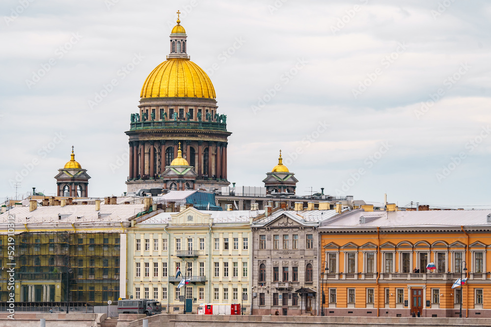 The huge golden dome of St. Isaac's Cathedral through the roofs of houses on the embankment of the Neva River in St. Petersburg in cloudy weather