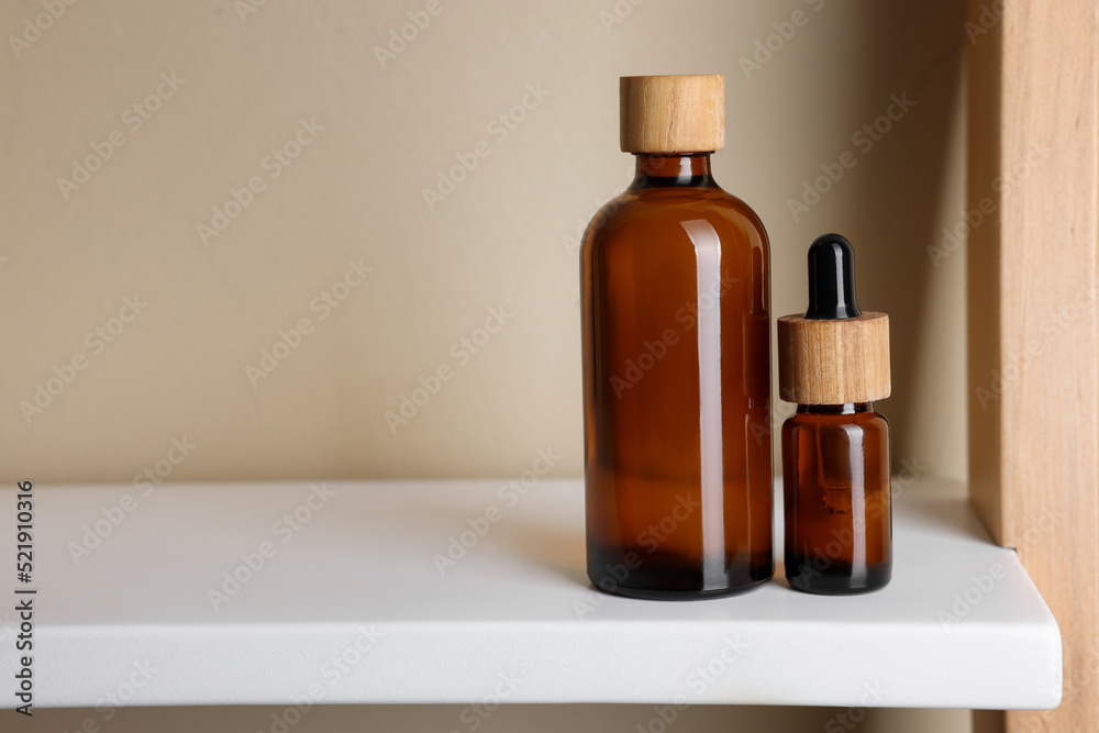 Glass bottles of cosmetic products on white shelf, space for text Glass bottles of cosmetic products on white shelf, space for text