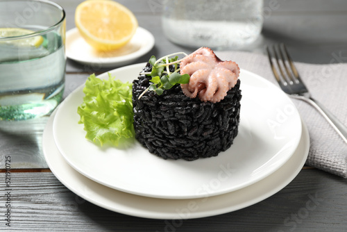 Delicious black risotto with baby octopus on grey wooden table