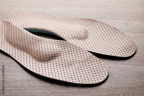 Beige orthopedic insoles on wooden background, closeup