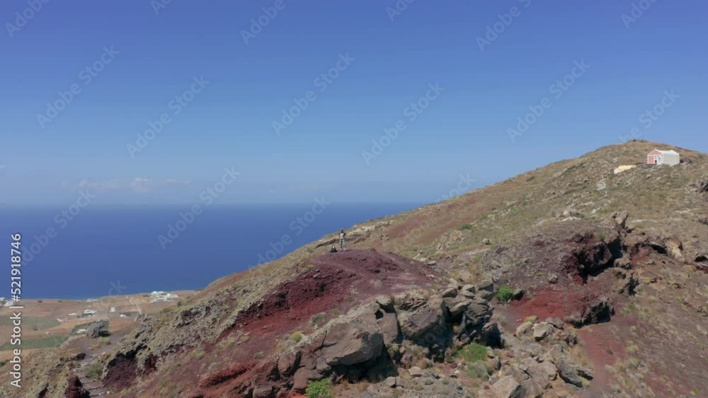 Aerial: Orbit shot of man standing on top of a hill in Santorini. Imerovigli in the background Aerial: Orbit shot of man standing on top of a hill in Santorini. Imerovigli in the background