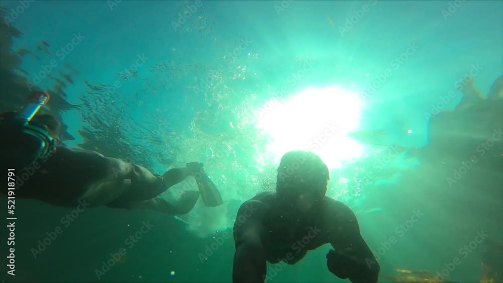 Two young men freediving along the Irish coastline against sunlight
