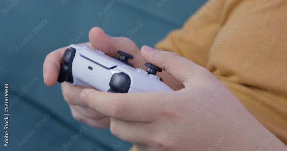 Person holds a controller for game console in hands and actively presses buttons, while playing difficult video game, close up. Gambling addiction or free time entertainments Person holds a controller for game console in hands and actively presses buttons, while playing difficult video game, close up. Gambling addiction or free time entertainments