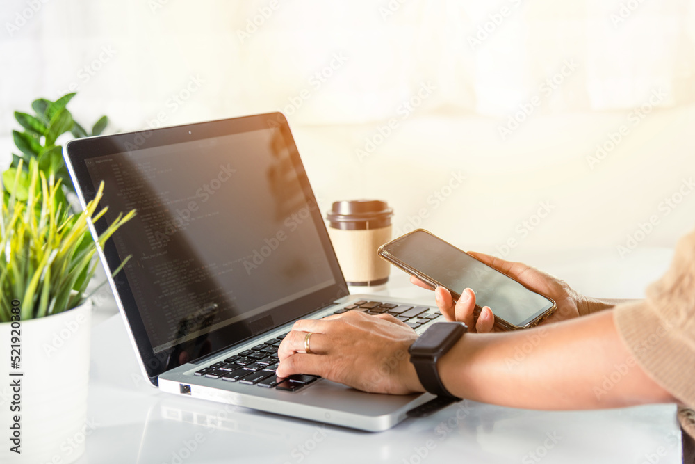 Fototapeta premium Software developer hands typing data coding programming javascript with laptop computer and mobile phone, Programmer woman looking smartphone program code at workplace, IT startup concept