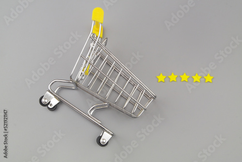 Shopping and feedback concept. Supermarket trolley with yellow stars under magnifying glass on gray background.