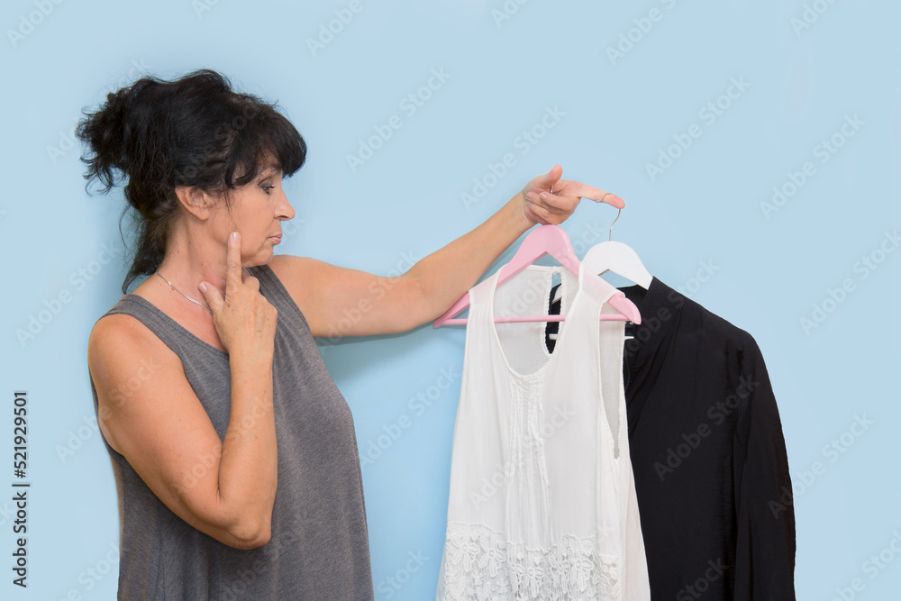 very beautiful woman looks thoughtfully at the hangers with clothes that she holds in her hands very beautiful woman looks thoughtfully at the hangers with clothes that she holds in her hands