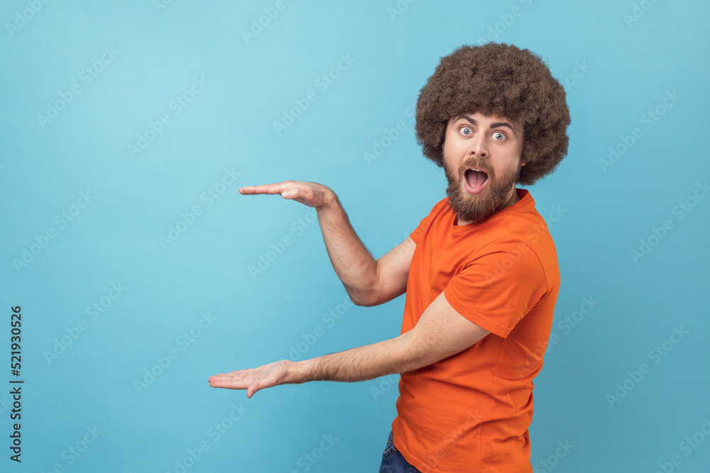 Φωτογραφία Portrait of amazed surprised man with Afro hairstyle presenting area for advertisement, looking at camera with big eyes and astonishment