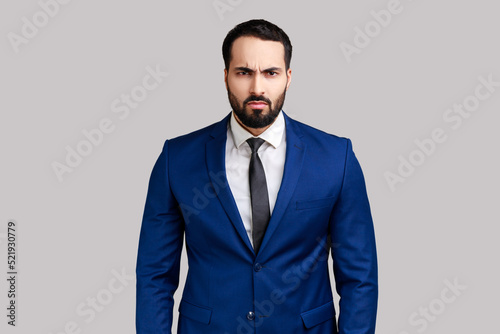 Portrait of bearded businessman looking at camera with angry face, having aggressive facial expression, wearing official style suit. Indoor studio shot isolated on gray background.