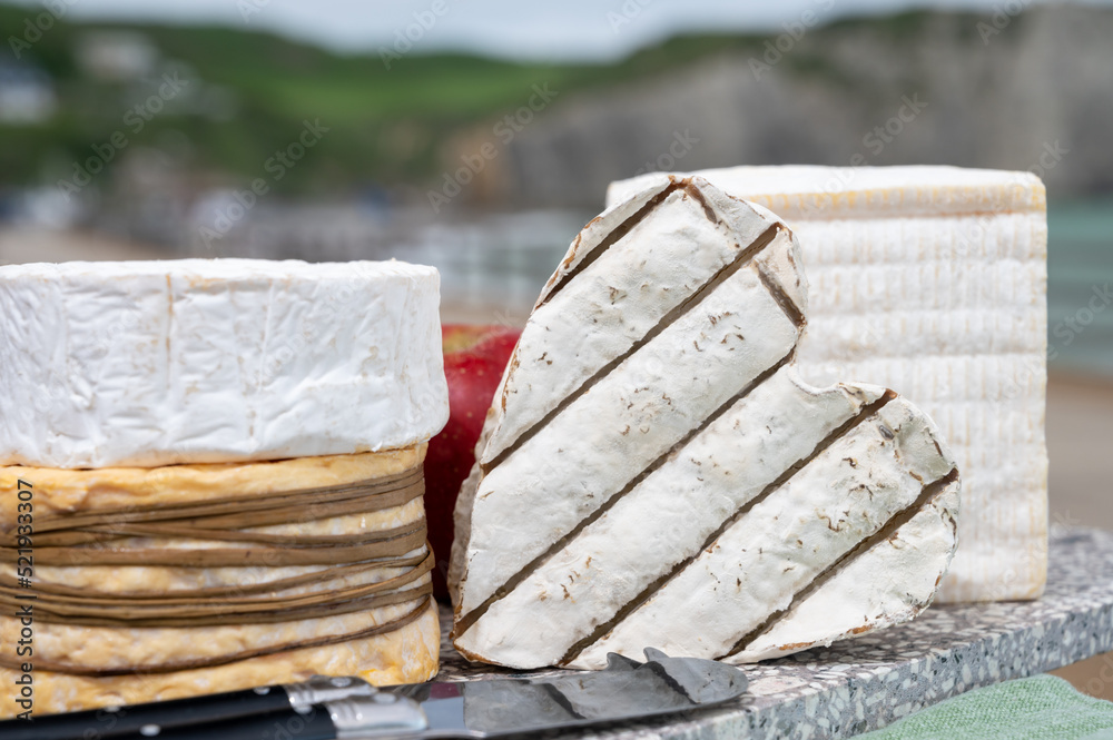 Four famous cheeses of Normandy, squared pont l'eveque, round camembert cow cheese, yellow livarot, heartshaped neufchatel and view on alebaster cliffs Porte d'Aval in Etretat, Normandy, France Four famous cheeses of Normandy, squared pont l'eveque, round camembert cow cheese, yellow livarot, heartshaped neufchatel and view on alebaster cliffs Porte d'Aval in Etretat, Normandy, France