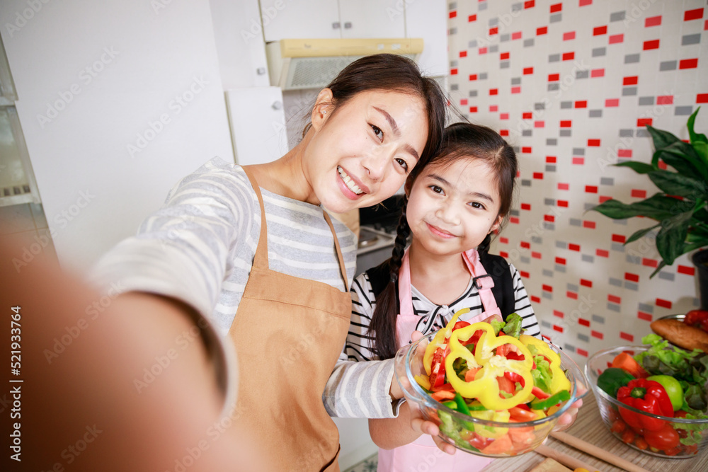 Mother and daughter preparing salad and taking a selfie by mobile phone. Leisure activity