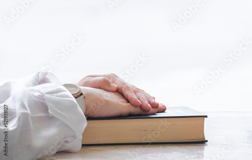 Close up of adult female hands praying on Holy Bible with softly bright light background