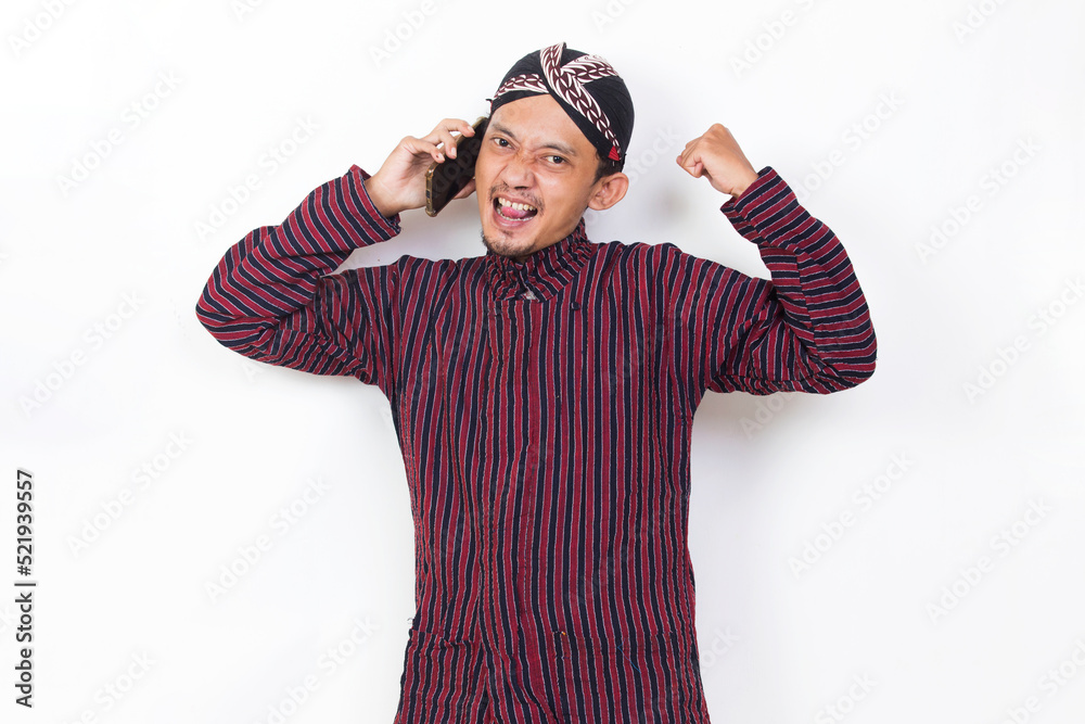 Happy joyful asian man with javanese traditional cloth lurik using mobile smartphone isolated on white background